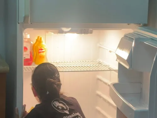 Ire Cleaning Services team member wiping down refrigerator shelves
